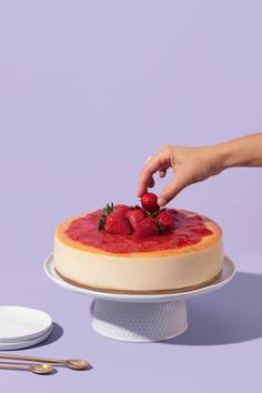 a person placing strawberries on top of a cheesecake