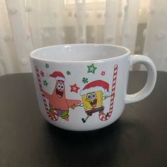 a white cup with spongebob and christmas characters on it sitting on a table