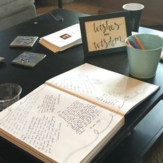 an open notebook sitting on top of a coffee table next to a cup and cell phone