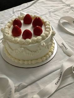 a white cake with strawberries on top sitting on a table next to measuring tape