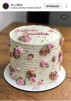 a white cake with pink frosting and roses on the top is sitting on a wooden table