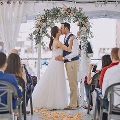 a bride and groom kissing in front of an outdoor wedding ceremony arch with flowers on it