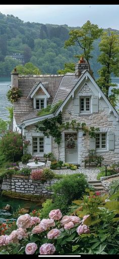 the house is surrounded by beautiful flowers and greenery, along with a lake in the background