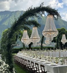 an outdoor dining table set up with chandeliers and white flowers on the table