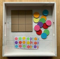 a white box with different colored circles and squares in it on top of a wooden floor