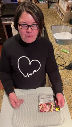 a woman in glasses is holding a piece of paper and looking at the camera with her hands