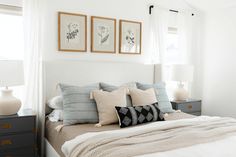 a bedroom with white walls and pillows on the bed, two framed pictures above the bed