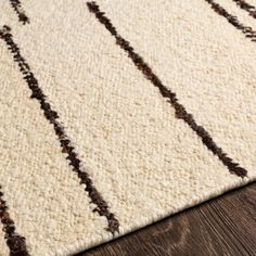 a white rug with brown lines on the top and bottom, sitting on a wooden floor