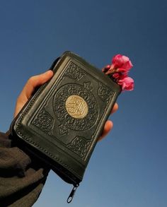 a person holding up a book with a flower in front of the camera and blue sky