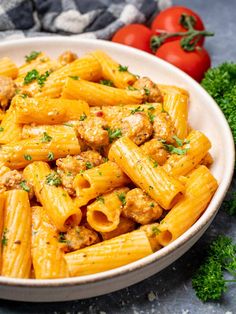 a bowl full of pasta with meat and parsley on the side next to tomatoes