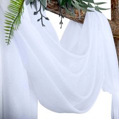 a white curtain draped over a tree branch with greenery on it's side