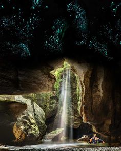 a man sitting under a waterfall in the middle of a forest filled with green lights