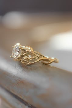 a yellow gold ring with a diamond on it's side sitting on a piece of wood