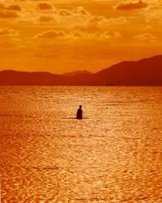 a person is sitting in the water at sunset