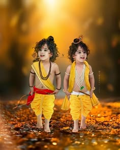 two young children dressed in yellow and red are walking through the leaves with each other