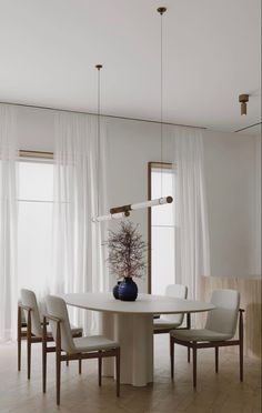 a dining room table with chairs and a vase on top of it in front of two windows