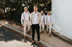 a group of men standing next to each other in front of a white wall and trees