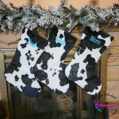 two black and white cow print christmas stockings hanging from a mantel with snow on it