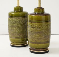 two green vases sitting next to each other on a white surface with gold accents