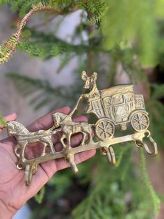 a hand holding a small brass horse and carriage ornament on a tree branch