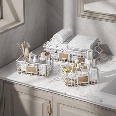 three white baskets with gold handles on a marble countertop next to towels and candles