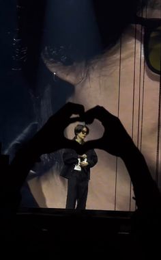 a man making a heart shape with his hands in front of him on stage at a concert