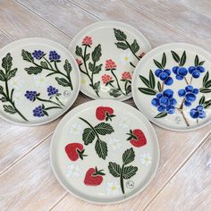 four plates with flowers painted on them sitting on a wooden table next to each other