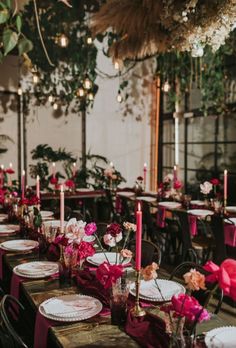 the tables are set with plates and place settings for guests to sit at, while pink flowers hang from the ceiling