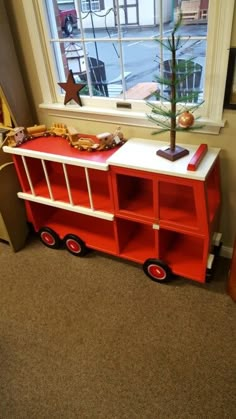 a toy firetruck next to a window with a christmas tree on top in front of it