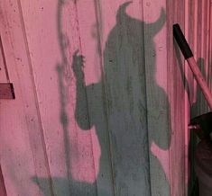 a shadow of a man holding an umbrella on the side of a wooden building next to a trash can