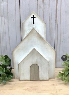 a small white church with a cross on the top and green plants next to it