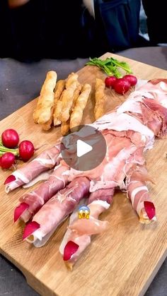 a wooden cutting board topped with meat and veggies next to bread sticks on top of a table