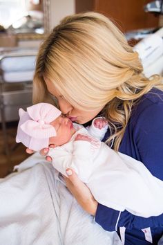 a woman holding a baby in her arms and kissing it's face with a pink bow on its head