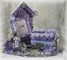 a small purple house sitting on top of a table next to flowers and a sign