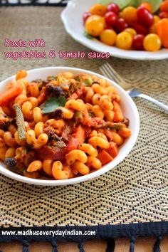 pasta with vegetables and tomato sauce in a white bowl on a woven place mat next to a salad