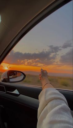 the person is driving in their car at sunset or dawn with his hand on the steering wheel