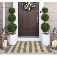 two potted topiary balls are on the front porch next to an entry door