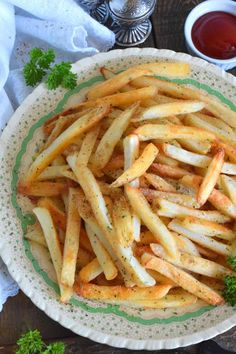 french fries with parsley in a green and white bowl on a wooden table top