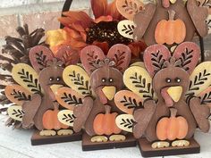 three wooden turkey figurines sitting in front of a basket filled with leaves and pumpkins