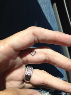 a woman's left hand with a small heart tattoo on the middle finger and a pink diamond ring