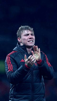 a man in black jacket standing on top of a soccer field holding his hands together