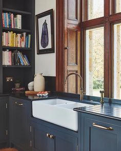 a kitchen sink sitting under a window next to a book shelf with books on it