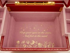 a pink box with gold writing on the inside and under it is filled with seashells