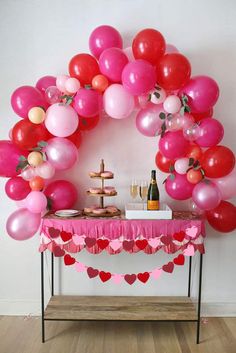 a table topped with lots of pink and red balloons next to a wine bottle on top of a wooden table