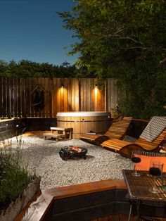 an outdoor hot tub surrounded by gravel and wooden benches with lights on the side of it