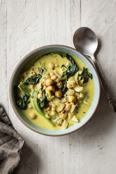 a bowl of soup with spinach and chickpeas in it on a white table