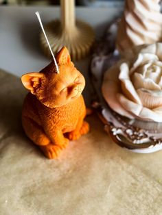 a cat figurine sitting on top of a table next to candles and flowers