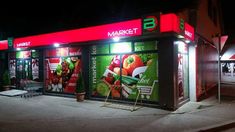 a market store at night with advertisements on the front and side walls, lit up by street lights