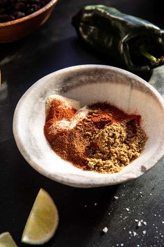 a bowl filled with spices sitting on top of a table next to sliced limes