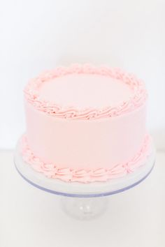 a pink frosted cake sitting on top of a white table next to a wall